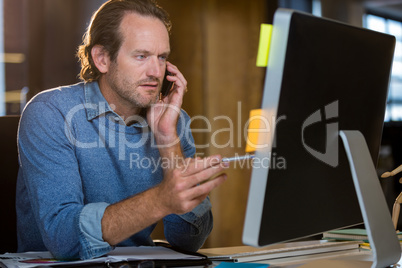 Businessman looking at monitor while talking on cellphone