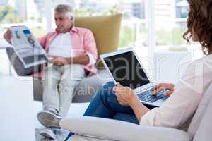 Woman using laptop while man reading newspaper