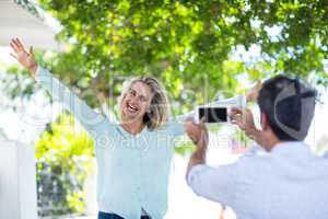 Man photographing cheerful woman against trees