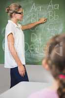 Smiling teacher teaching kids on chalkboard in classroom