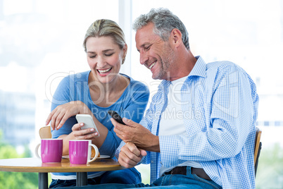 Smiling couple using mobile phones at cafe