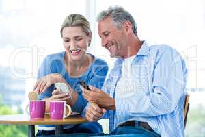Smiling couple using mobile phones at cafe