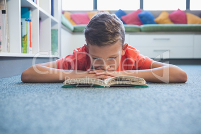 Schoolboy lying on floor and reading a book in library