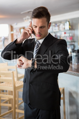 Businessman checking time while talking on the mobile phone