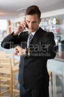 Businessman checking time while talking on the mobile phone