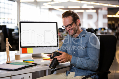 Businessman holding camera while sitting by desk