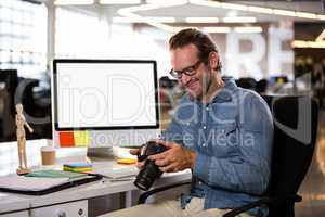 Businessman holding camera while sitting by desk