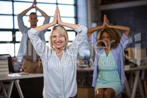 Businesswoman practicing yoga with coworkers