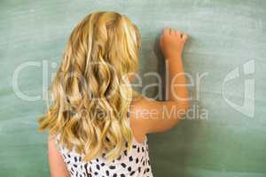 Rear view of school girl writing on chalkboard in classroom