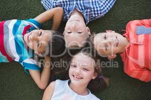 Smiling schoolkids lying on grass in campus