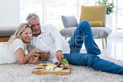 Smiling couple having food while lying on rug