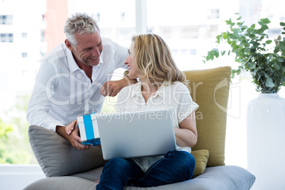 Smiling man giving gift to woman holding laptop