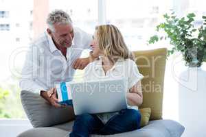 Smiling man giving gift to woman holding laptop