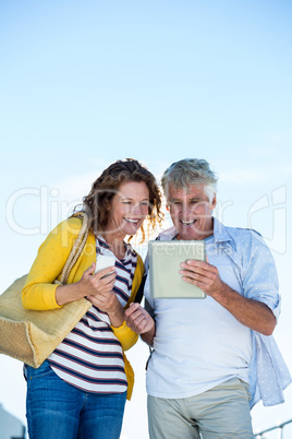 Happy couple using digital tablet against sky