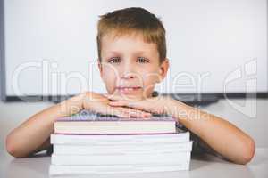 Portrait of smiling boy leaning on stack of books in class room