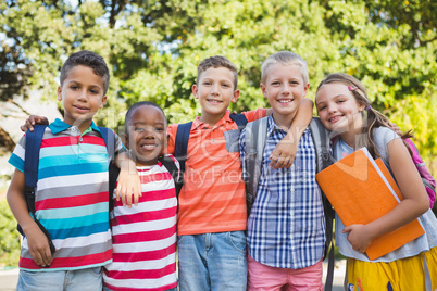 Smiling schoolkids standing with arms around in campus