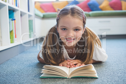 Schoolgirl lying on floor and reading a book in library