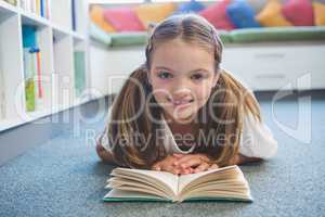 Schoolgirl lying on floor and reading a book in library