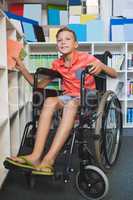 Disabled schoolboy selecting a book from bookshelf in library