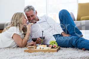 Smiling woman feeding food to man while lying on rug