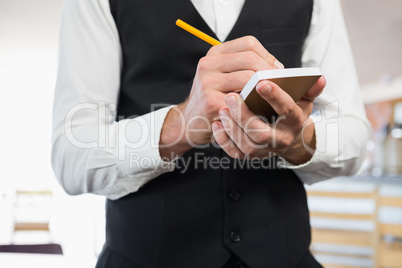 Mid section of waiter writing order on notepad