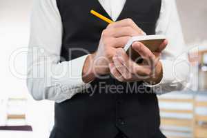 Mid section of waiter writing order on notepad