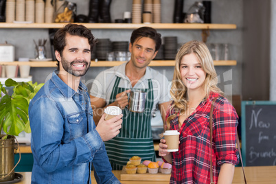 Portrait of smiling couple standing at counter holding cup of co