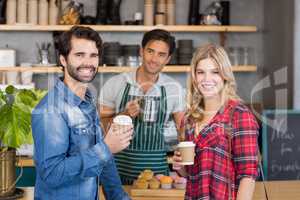 Portrait of smiling couple standing at counter holding cup of co