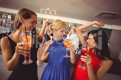 Female friends holding glass of cocktail while dancing