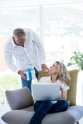 Man giving gift to woman holding laptop