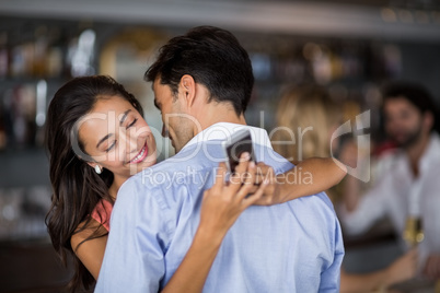 Woman checking mobile phone while embracing man