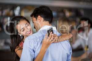 Woman checking mobile phone while embracing man