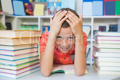 Schoolboy sitting on table and reading book in library