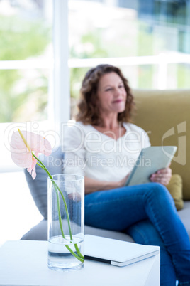 Flower in vase with mature woman holding tablet