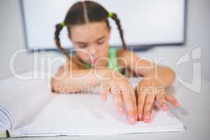 Schoolgirl reading a braille book in classroom