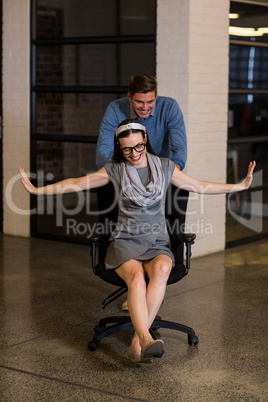 Man pushing female colleague sitting on chair