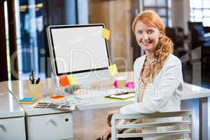 Businesswoman smiling while sitting by computer desk