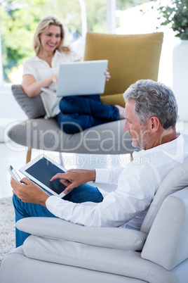 Mature man using tablet while woman holding laptop