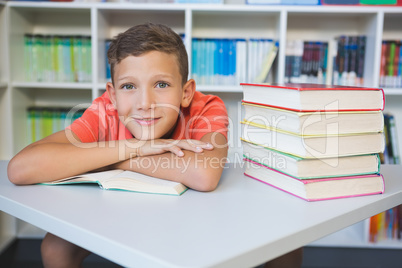 Portrait of schoolboy leaning on a book in library