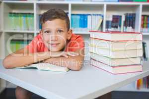 Portrait of schoolboy leaning on a book in library