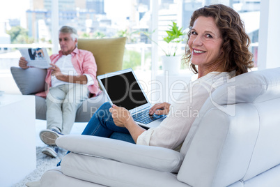 Smiling woman with laptop while mature man reading newspaper