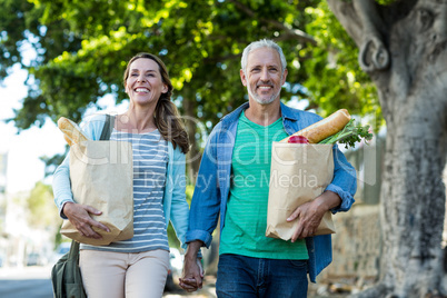 Mature couple holding shopping bags by tree