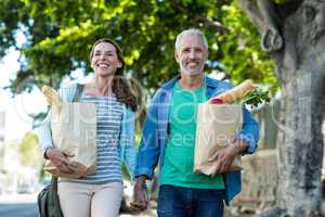 Mature couple holding shopping bags by tree