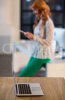 Laptop on table with woman standing in background at office