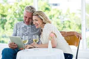 Smiling mature couple using digital tablet with wine on table