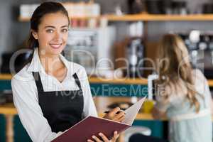 Portrait of smiling waitress writing in a file