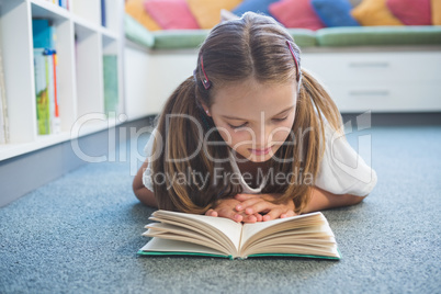 Schoolgirl lying on floor and reading a book in library