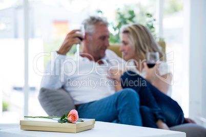 Rose and gift box on table with couple having red wine