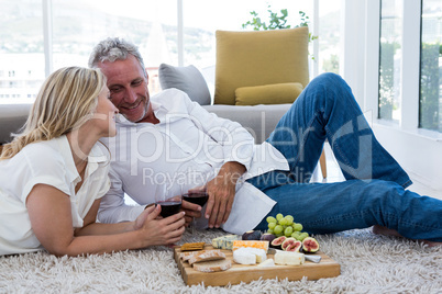 Romantic couple with red wine and food while lying on rug