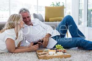 Romantic couple with red wine and food while lying on rug